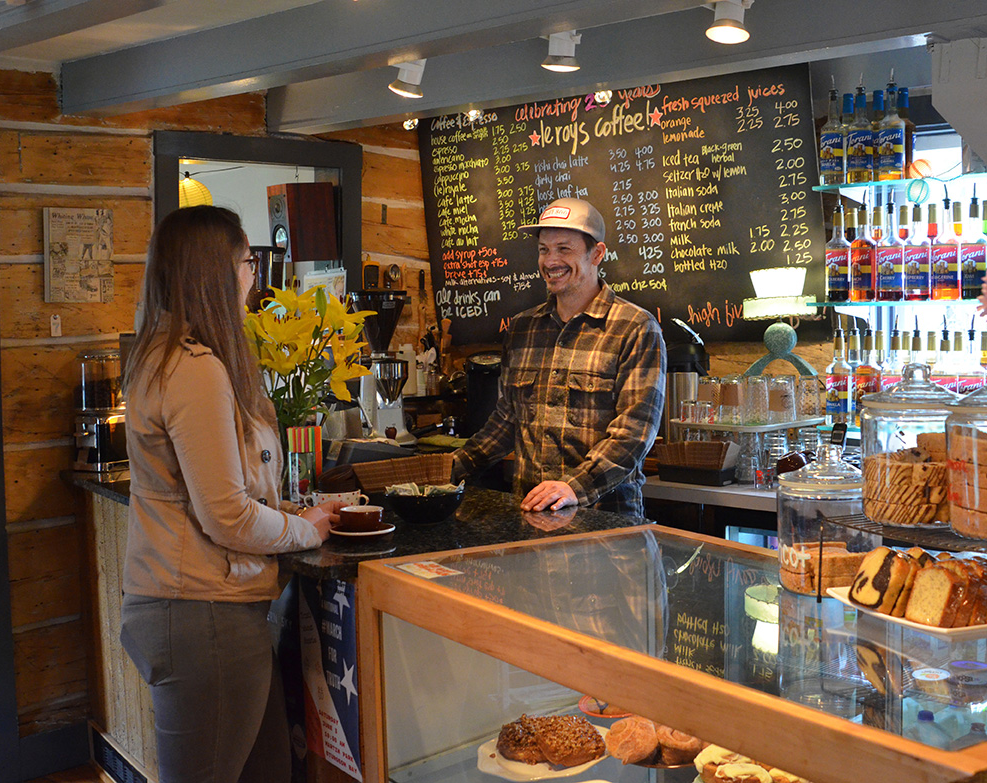 woman ordering coffee at a counter from a man wearing a hat